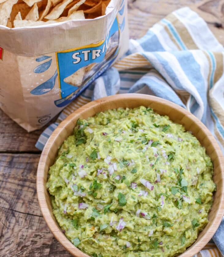 "Bowl of green chile guacamole with tortilla chips and lime wedges on rustic table"