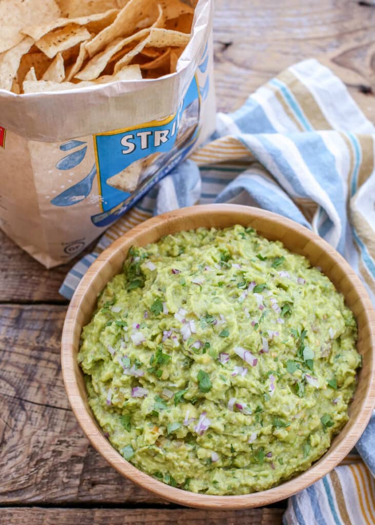"Bowl of green chile guacamole with tortilla chips and lime wedges on rustic table"